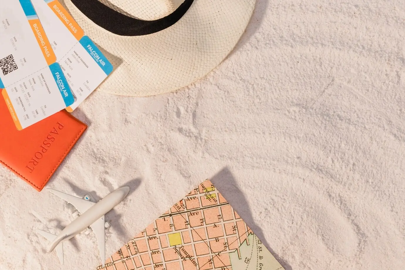 Ein Flugzeug und Tickets sowie ein Hut und eine Karte auf Sand.